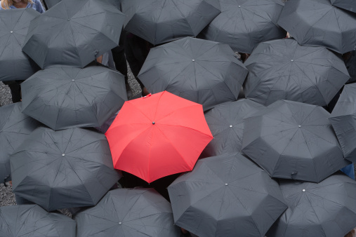 One red umbrella at center of multiple black umbrellas